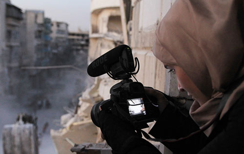woman with video camera looks through the monitor from a window down on a destroyed street