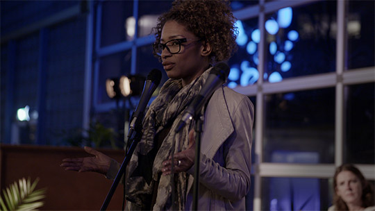 Sylvana Simon standing in front of a microphone.