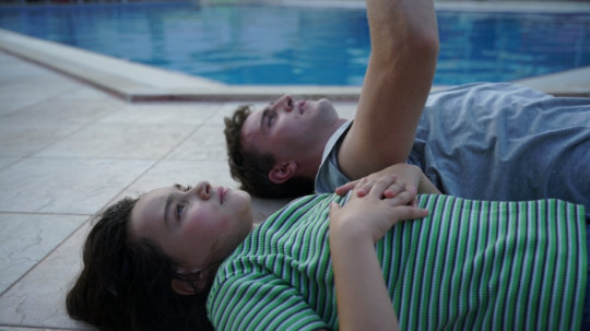 Mann und Mädchen liegen am Pool auf dem Rücken und schauen in den Himmel
