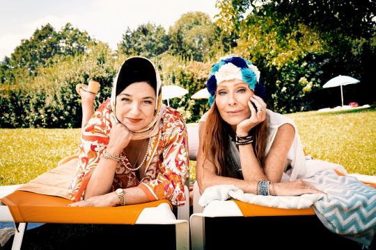 Filmstill Freibad, zwei Frauen liegen auf einem Handtuch, eine hat eine Kopftuch auf, die andere eine Badekappe