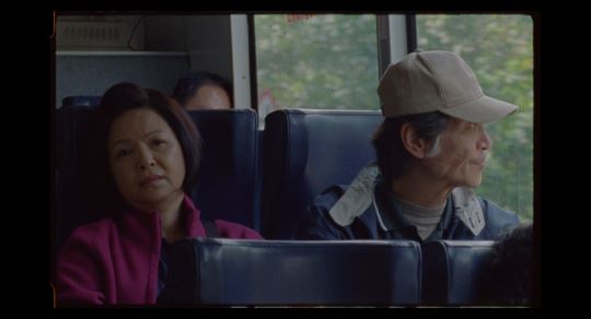 Ein alter Mann mit Schirmmütze sitzt in einem Bus und schaut aus dem Fenster. Neben Ihm sitzt eine Frau